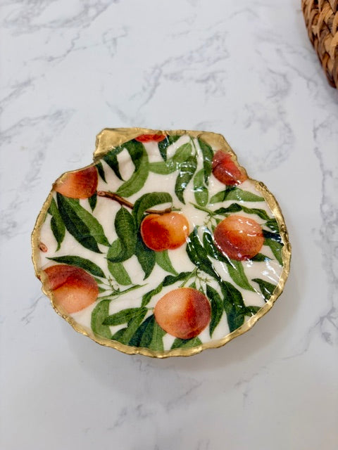 A small decorative dish with an irregular scalloped edge, featuring peaches on a white background with a gold-toned distressed rim.