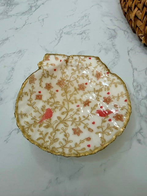 A small decorative dish with an irregular scalloped edge, featuring a floral  pattern with birds on a white background with a gold-toned distressed rim.