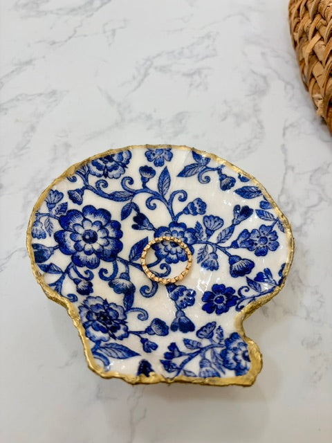 A small decorative dish with an irregular scalloped edge, featuring a floral  pattern on a white background with a gold-toned distressed rim.