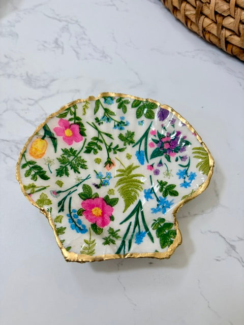 A small decorative dish with an irregular scalloped edge, featuring a floral  pattern on a white background with a gold-toned distressed rim.