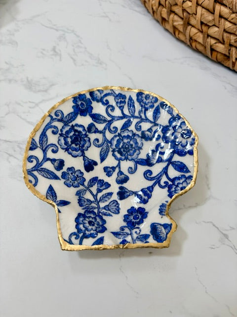 A small decorative dish with an irregular scalloped edge, featuring a blue floral and vine pattern on a white background with a gold-toned distressed rim.