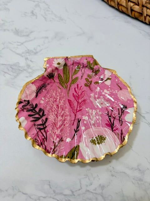 A small decorative dish with an irregular scalloped edge, featuring a floral  pattern on a pink background with a gold-toned distressed rim.