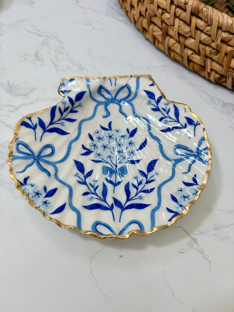 A small decorative dish with an irregular scalloped edge, featuring a floral  pattern on a white background with a gold-toned distressed rim.