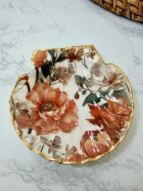 A small decorative dish with an irregular scalloped edge, featuring a floral  pattern on a white background with a gold-toned distressed rim.