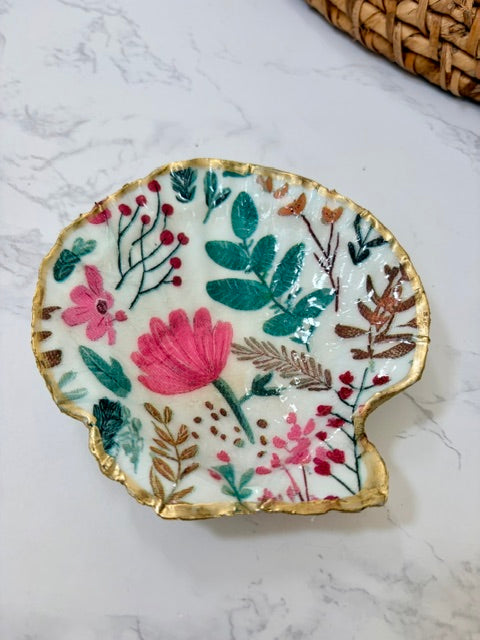 A small decorative dish with an irregular scalloped edge, featuring a floral  pattern on a white background with a gold-toned distressed rim.