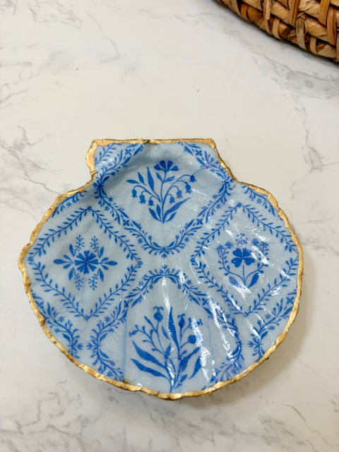 A small decorative dish with an irregular scalloped edge, featuring a floral  pattern on a blue background with a gold-toned distressed rim.