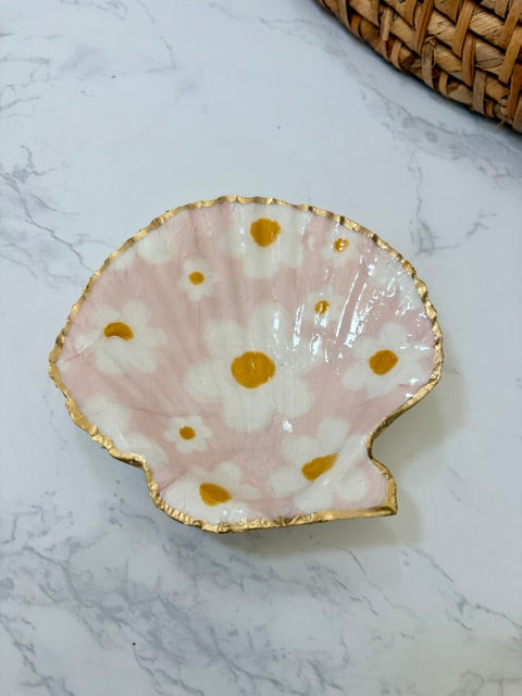 A small decorative dish with an irregular scalloped edge, featuring a floral  pattern on a pink background with a gold-toned distressed rim.