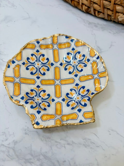A small decorative dish with an irregular scalloped edge, featuring a cross  pattern on a white background with a gold-toned distressed rim.