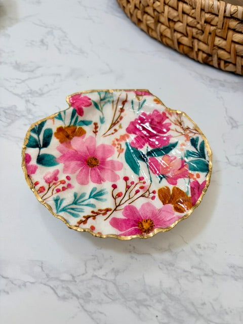 A small decorative dish with an irregular scalloped edge, featuring a floral  pattern on a white background with a gold-toned distressed rim.