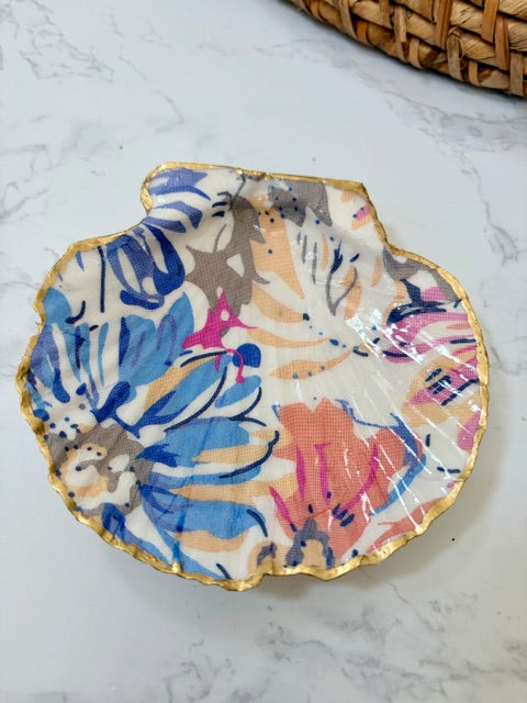 A small decorative dish with an irregular scalloped edge, featuring a floral  pattern on a white background with a gold-toned distressed rim.