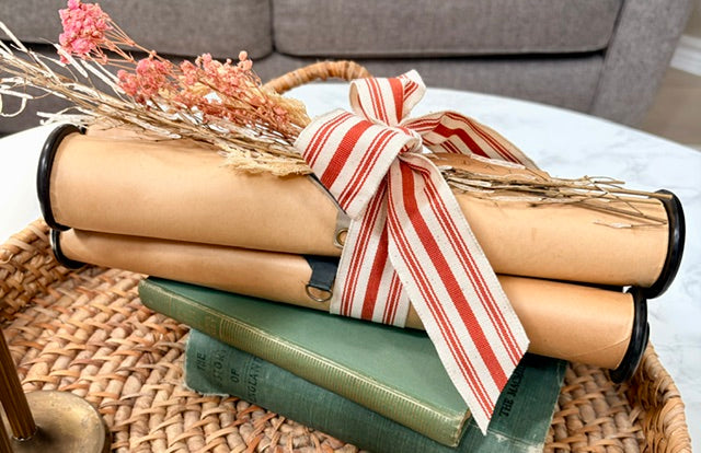 Bundle of three piano rolls with dried florals, and striped fabric bow on a stack of books.