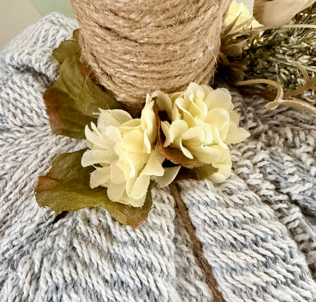 Close up of cream florals with green leaves on a knitted pumpkin.