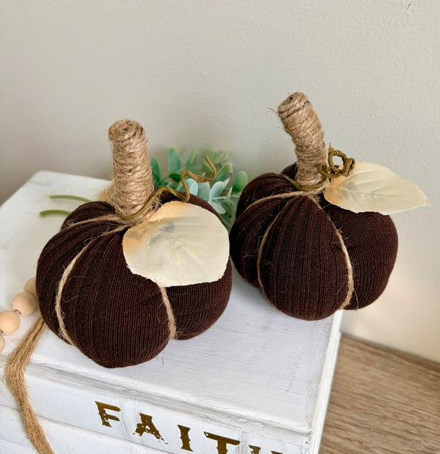 Two dark brown knitted fabric pumpkins with natural jute stems and cream paper leaves, displayed on a white decorative box.