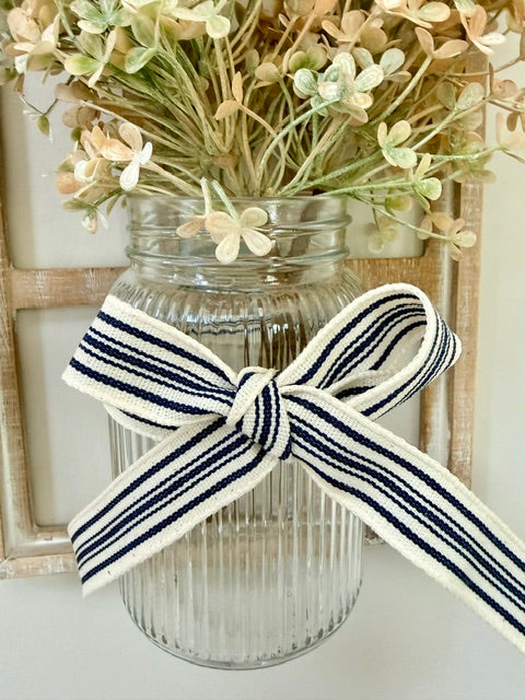 Close up of a jar holding florals decorated with a blue and white striped bow.