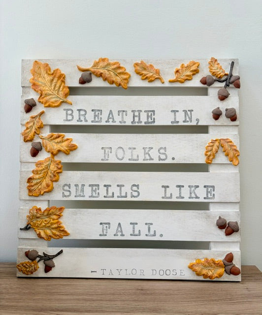 A rustic decorative wooden sign with white painted slats and the quote 'BREATHE IN,folks. SMELLS LIKE FALL.