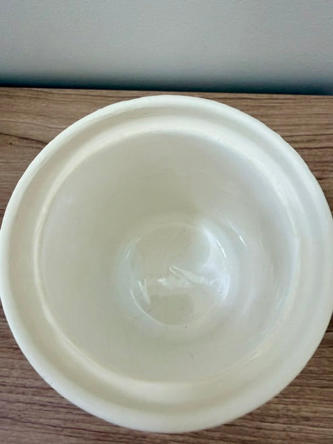 A white ceramic bowl photographed from directly above on a wooden tabletop against a plain wall.