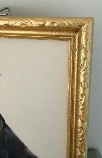 Close-up of an ornate gold picture frame corner against a light gray wall.
