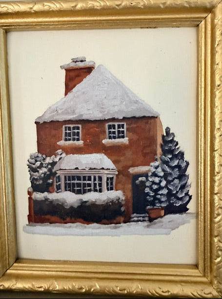 A framed painting of a snow-covered brick house with dark chimneys and trees, set in a wide cream mat and an ornate gold frame.