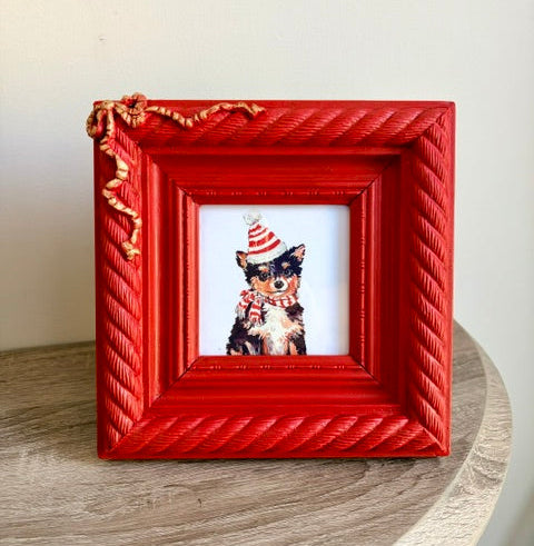 Red braided frame with gold bow in top corner and festive puppy with a striped hat and scarf.