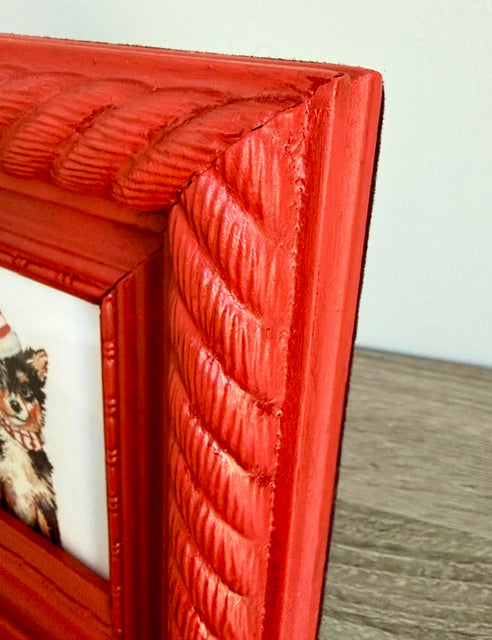 A close-up of a red decorative picture frame with a textured rope-like border design, showing part of a printed pet photo inside.