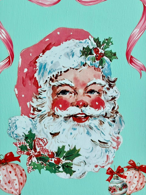 A festive Christmas-themed print featuring a painted Santa Claus face with a red hat, white beard, and holly accents on a turquoise background with pink ribbon and ornament illustrations.