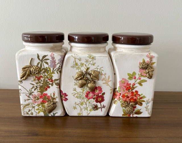 Three decorative ceramic jars with floral patterns on a wooden surface.