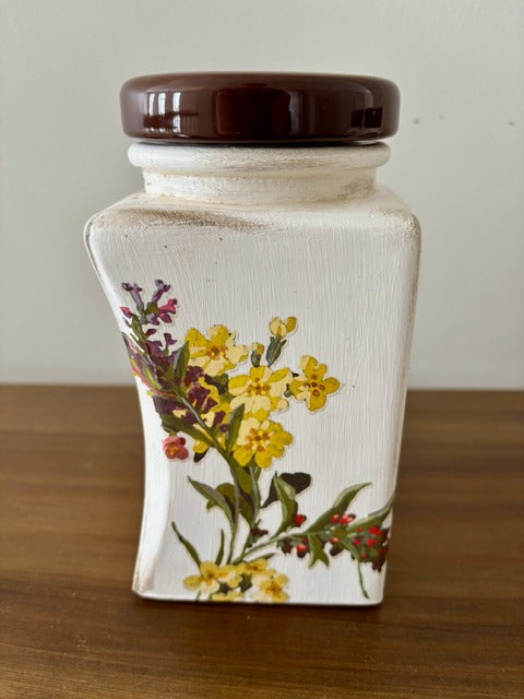 Ceramic jar with floral design and brown lid on a wooden surface