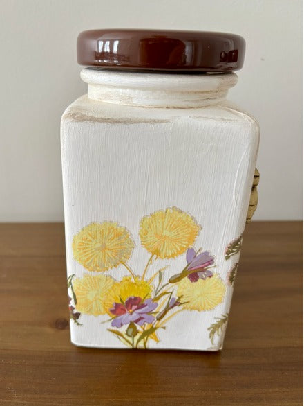 Decorative jar with floral design and brown lid on a wooden surface
