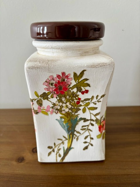 Decorative jar with floral design and brown lid on a wooden surface