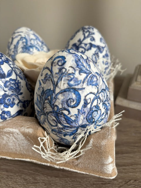 Decorative eggs with blue floral patterns in an egg carton