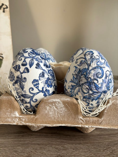 Decorative eggs with blue floral patterns in an egg carton