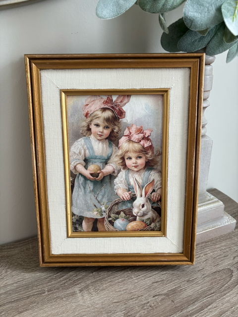 Framed artwork of two children with a rabbit on a white surface.