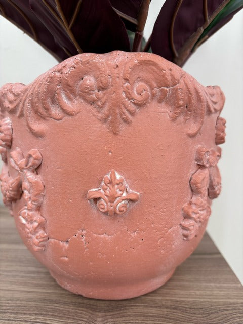 Decorative terracotta pot with intricate designs on a wooden surface.