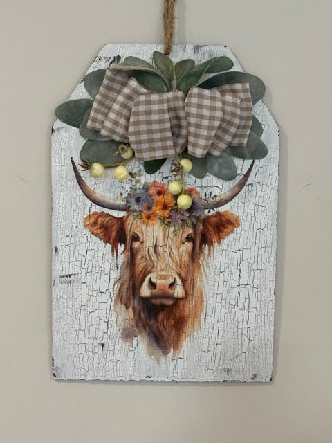 Decorative sign with a cow's head, flowers, and a bow on a white background