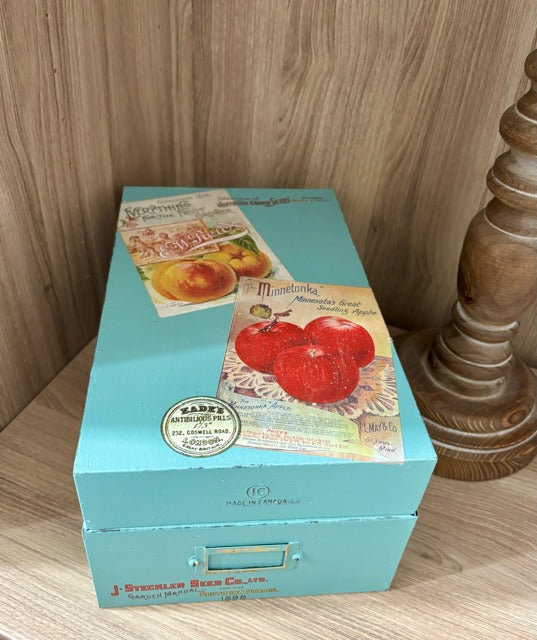 Teal box with vintage-style fruit illustrations on a wooden surface