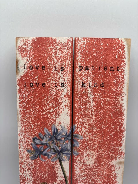 Wooden plaque with text 'love is patient, love is kind' and a floral design on a gray background