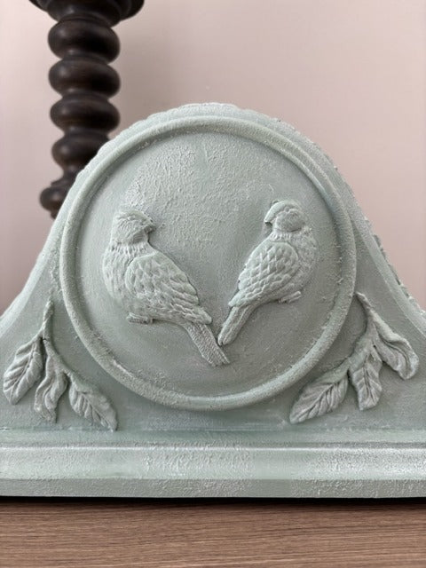 Decorative wall piece with embossed birds and leaf design on a light green background.