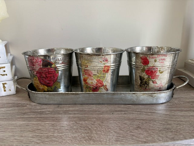 Three metal buckets with floral decal on a tray