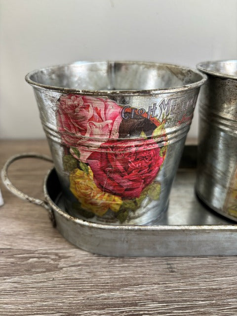 Three metal buckets with floral decal on a tray
