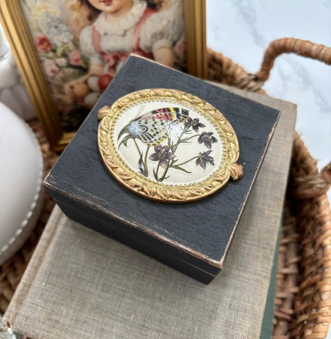Decorative box with floral design on top, placed on a textured surface 