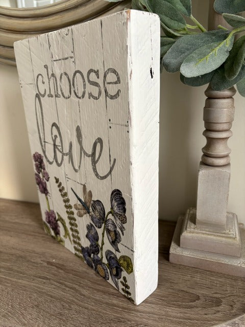 Decorative sign with 'choose love' text and floral design on a wooden surface.