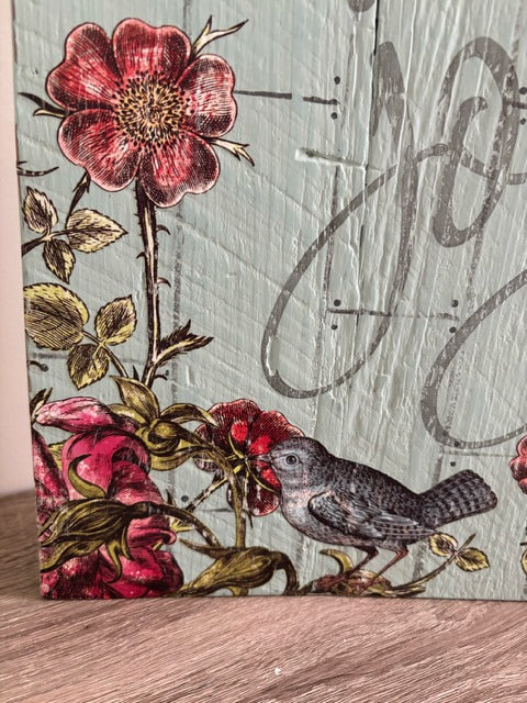 Decorative sign with floral design and bird on a wooden surface