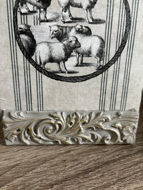 Decorative clay strip with intricate design on a wooden surface, with a black and white patterned fabric in the background featuring sheep illustrations.