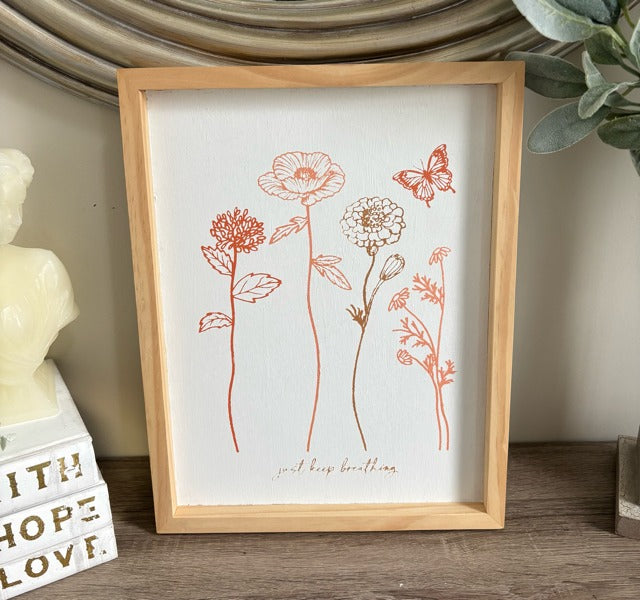Framed artwork with floral illustrations on a shelf with decorative items.