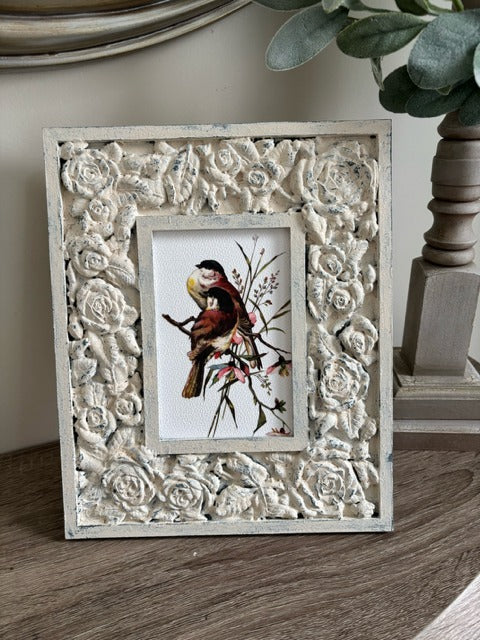 Decorative frame with floral patterns holding a print of a bird on a branch.