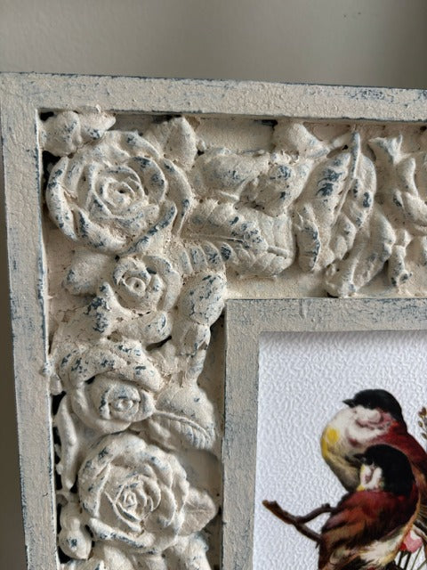 Decorative frame with floral patterns holding a print of a bird on a branch.