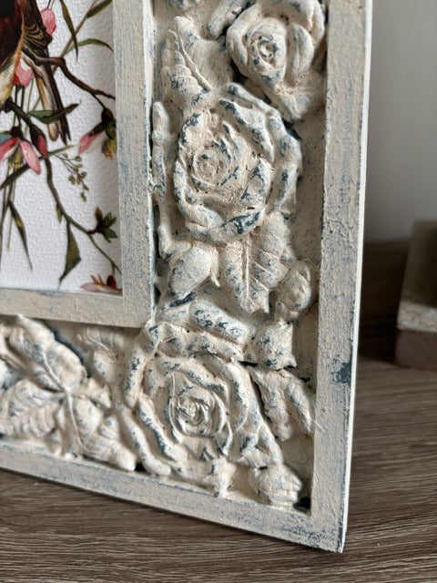 Decorative frame with floral patterns holding a print of a bird on a branch.