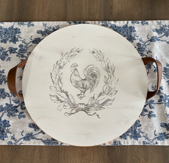 Round wooden tray with a rooster design on a floral tablecloth