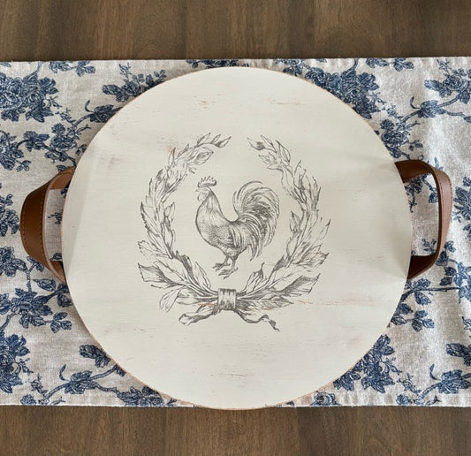 Round wooden tray with a rooster design on a floral tablecloth