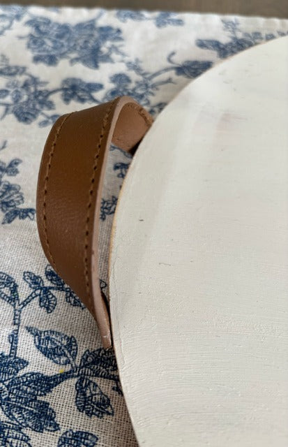 Close-up of a white tray with a brown leather strap on a patterned fabric background
